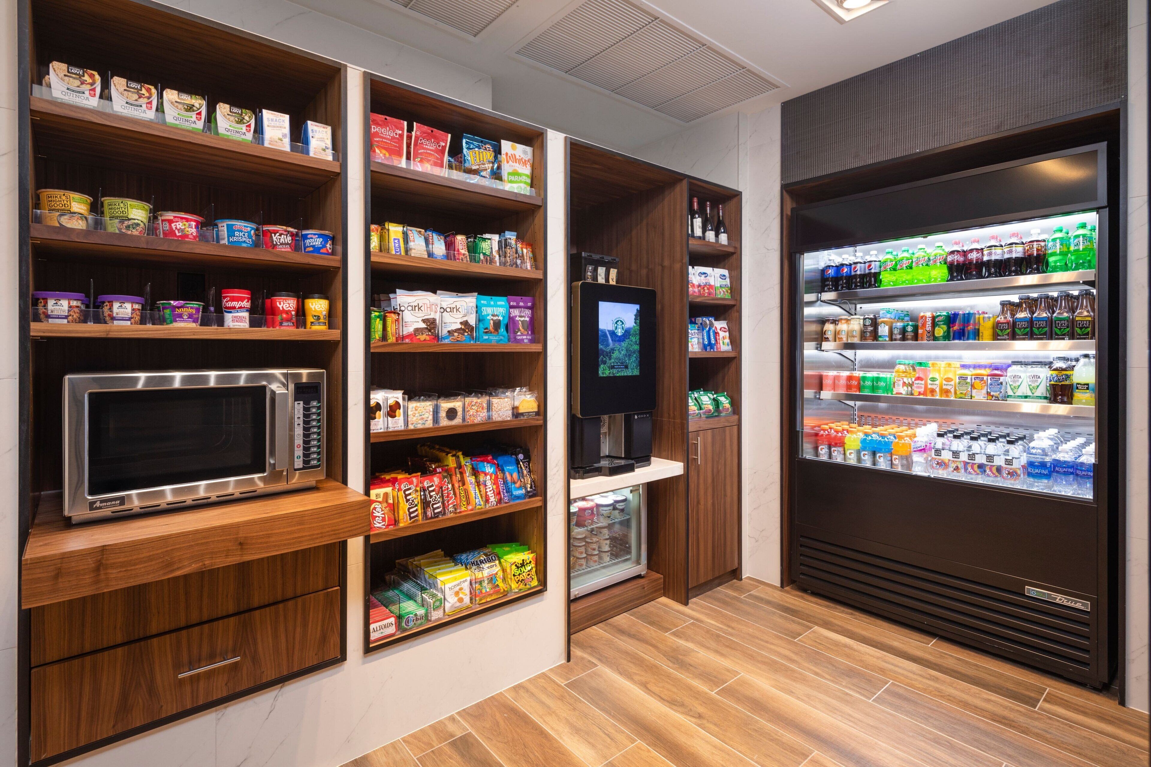 Een kitchenette met een magnetron, planken vol snacks, een koelkast en een televisie.