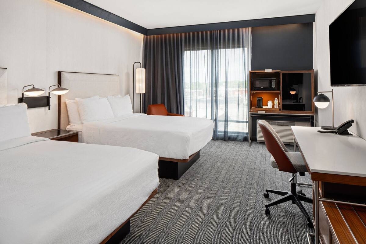 Une chambre d’hôtel avec deux lits, un bureau, une chaise, une télévision et un mini-bar.