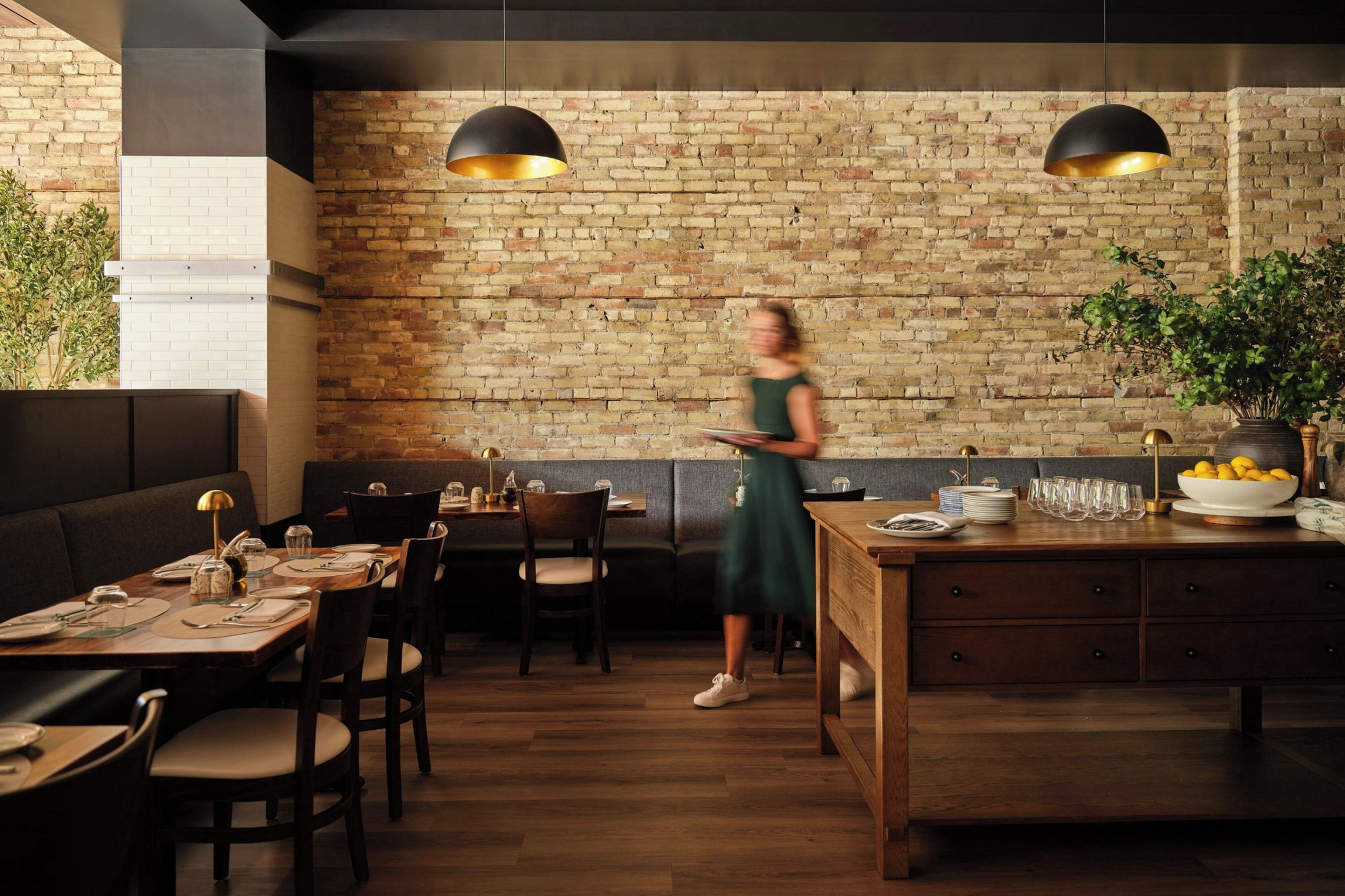 Een restaurantinterieur met bakstenen muren, houten tafels en zwarte hanglampen.