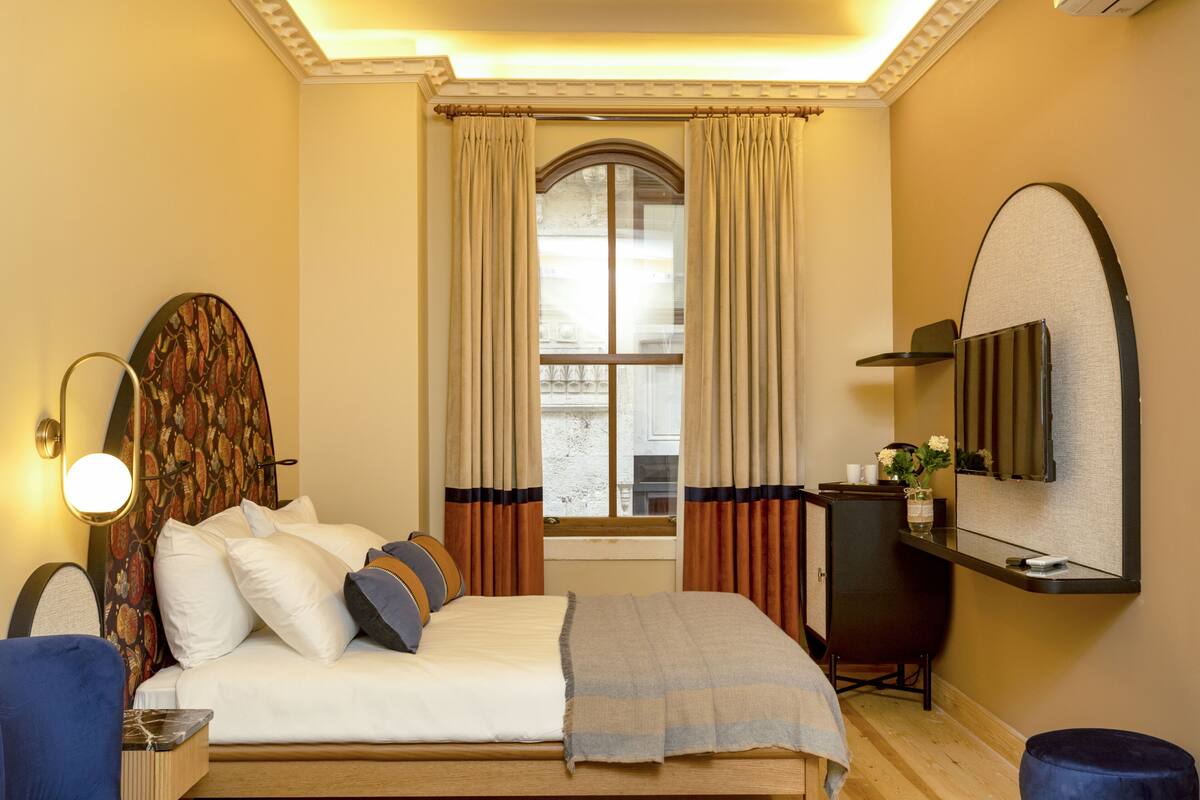 A hotel room with a bed, a desk, a chair, a TV, and a window with curtains.