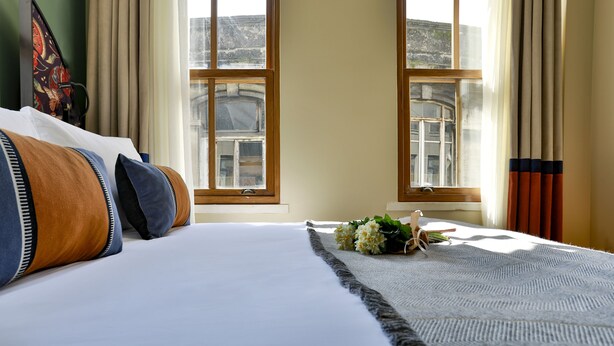 Ein Hotelzimmer mit einem großen Bett, zwei Fenstern und Blick auf die Stadtlandschaft.