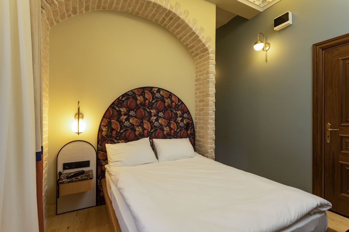 A neatly made bed with a patterned headboard, a bedside table with a lamp, and a small shelf with a telephone.