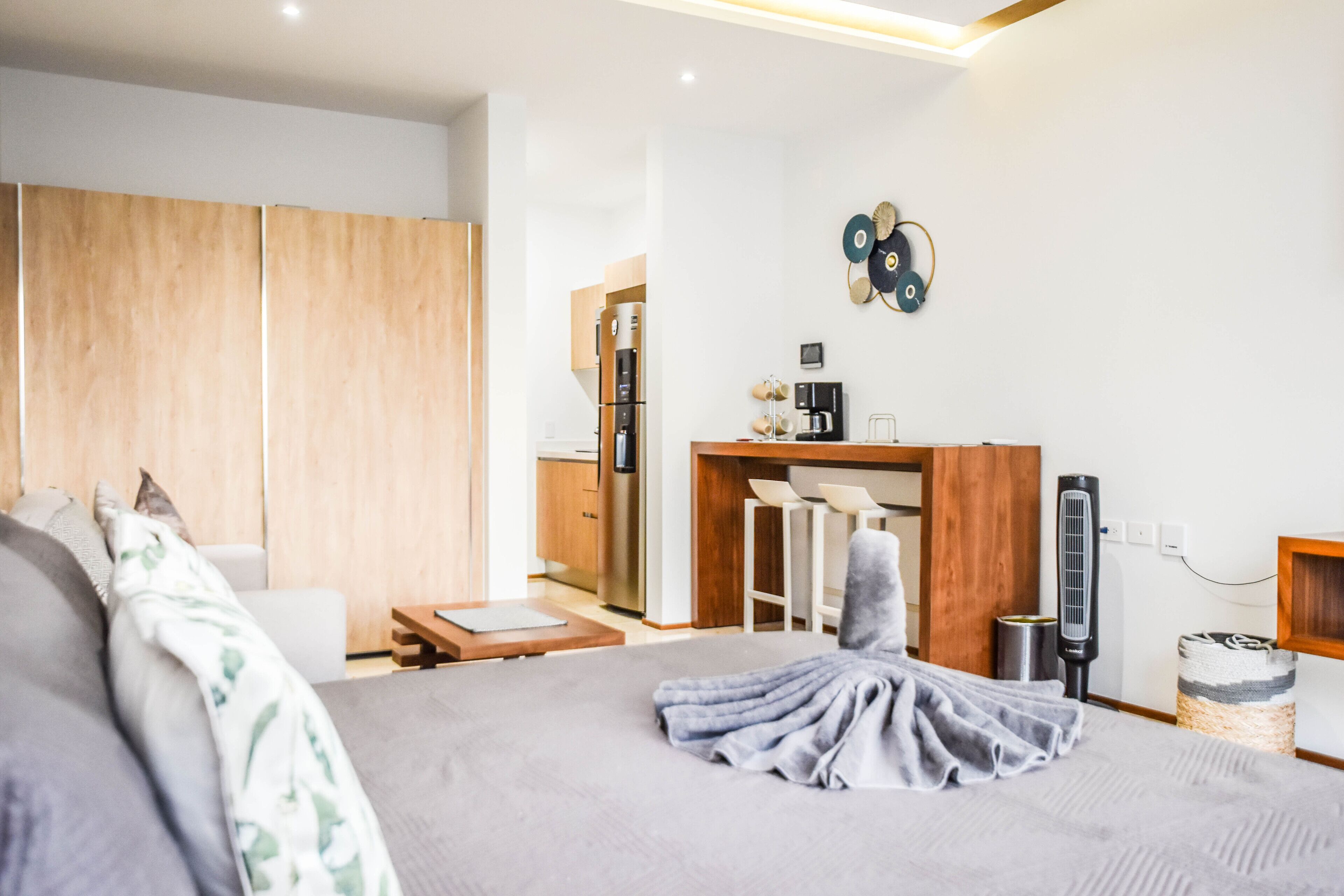 A modern bedroom with a large bed, a desk, and a kitchenette.