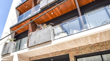 Un immeuble à plusieurs étages doté d’une architecture moderne, avec des balcons ornés de plantes, une entrée imposante agrémentée d’un logo et de grandes fenêtres.