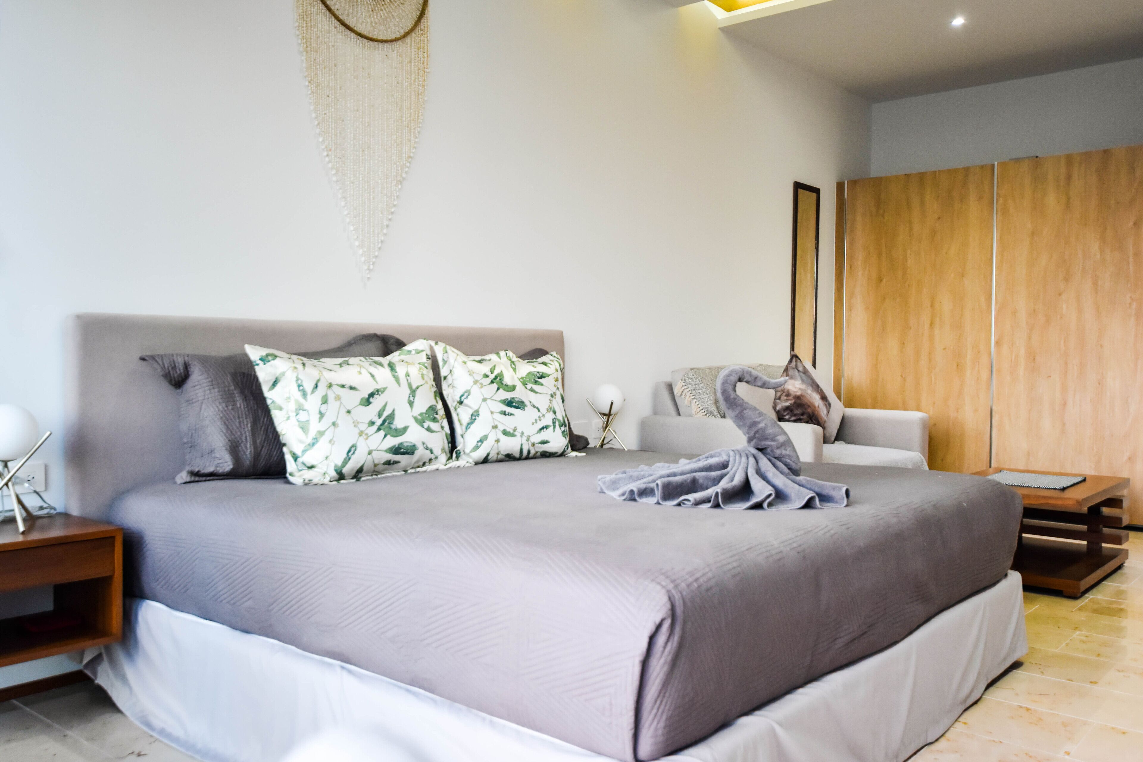 A modern bedroom with a large bed, a wooden wardrobe, and a bedside table with a lamp.