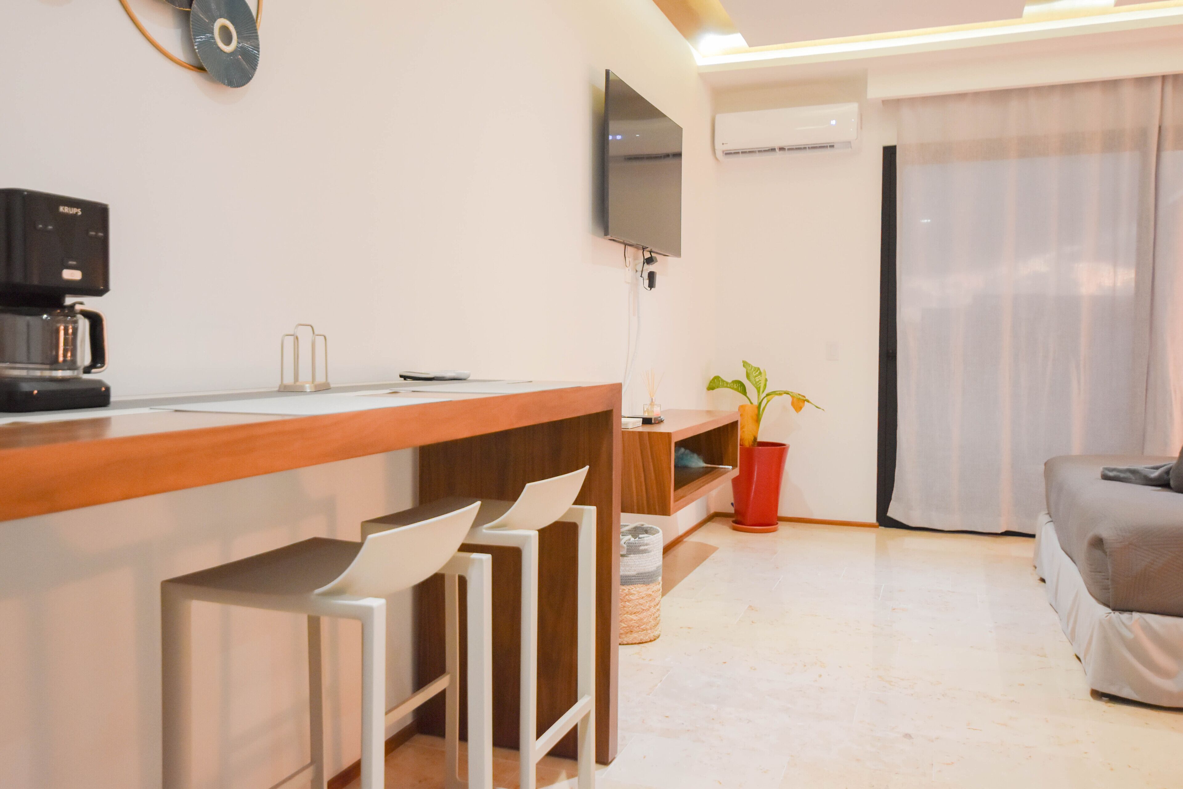 Una cocina moderna con cafetera, un televisor de pantalla plana en la pared y un comedor con mesa de madera y taburetes de bar.