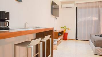 Una cocina moderna con cafetera, un televisor de pantalla plana en la pared y un comedor con mesa de madera y taburetes de bar.