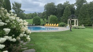 Ein Swimmingpool mit einer Laube und gelben Stühlen in einem angelegten Garten.