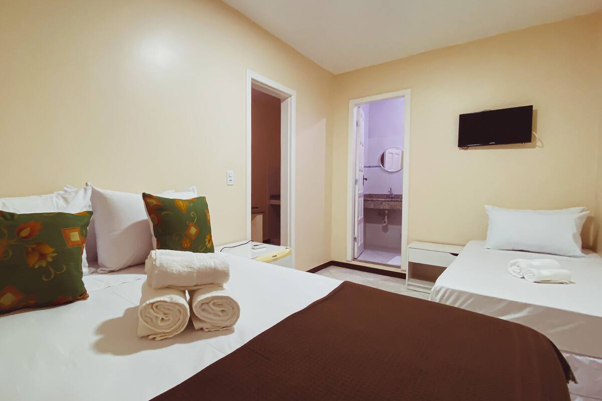 Ein Hotelzimmer mit zwei Betten, jeweils mit weißen Leinen und Kissen, einer braunen Tagesdecke und einem an der Wand befestigten Fernseher.