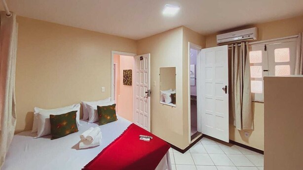 Una habitación de hotel con una cama, una manta roja, un espejo y un armario.