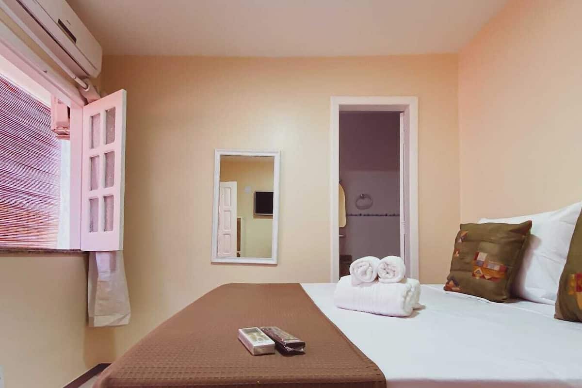 Ein Hotelzimmer mit Bett, Nachttisch, Spiegel und einem Fenster mit Jalousien.