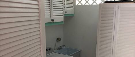 Een wasserette met een wasmachine, een wastafel en een droogrek.