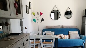 Una habitación con una mesa de comedor, sillas, un sofá azul, un ventilador de techo y un mueble con objetos decorativos.