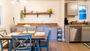 A modern kitchen with wooden countertops, a built-in dishwasher, and a dining area with blue chairs and a wooden table. - Madrona's Guesthouse- Spacious 2BR with Huge Fenced Yard (North Charleston)