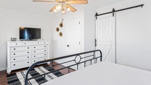 Un dormitorio con cama, ventilador de techo, cómoda, televisor y puerta corredera.