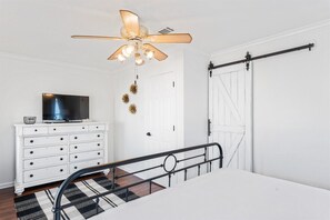 A bedroom with a bed, a ceiling fan, a dresser, a television, and a sliding door.