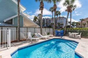 A swimming pool with lounge chairs and a table, surrounded by palm trees and a white fence.