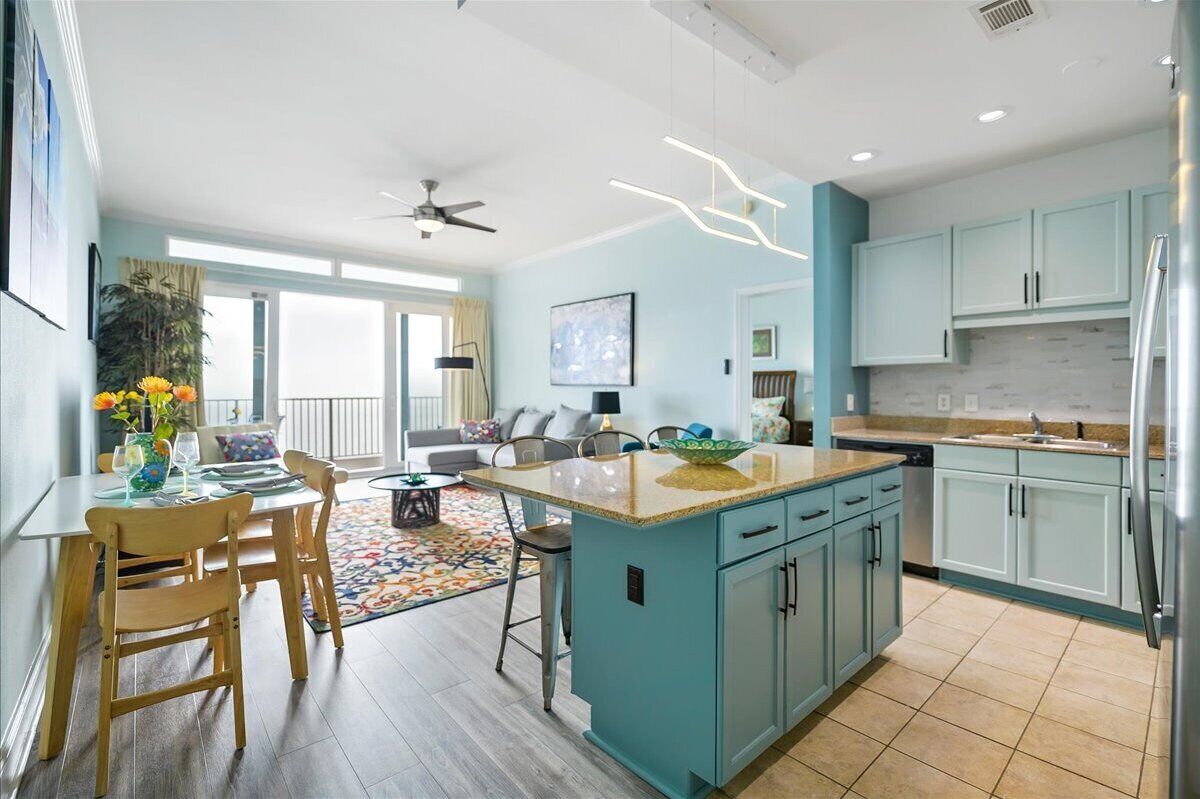 Une cuisine moderne avec des meubles de couleur turquoise, un îlot central et un coin repas comprenant des chaises et une table en bois.