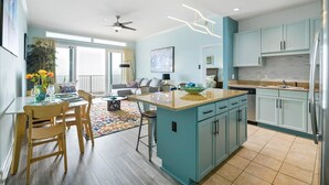 A modern kitchen with teal cabinets, a central island, and a dining area with wooden chairs and a table. - Aqua Penthouse 2br/2ba with Infinite Ocean Views (Panama City Beach)