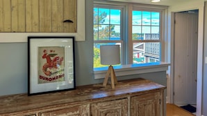 Una habitación con un armario de madera rústica, un cartel antiguo enmarcado y una ventana con vistas a un muelle y edificios.