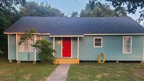 A single-story house with a red door, a small porch, and a yellow hose on the side. - Brightly Homely House  (Odem)