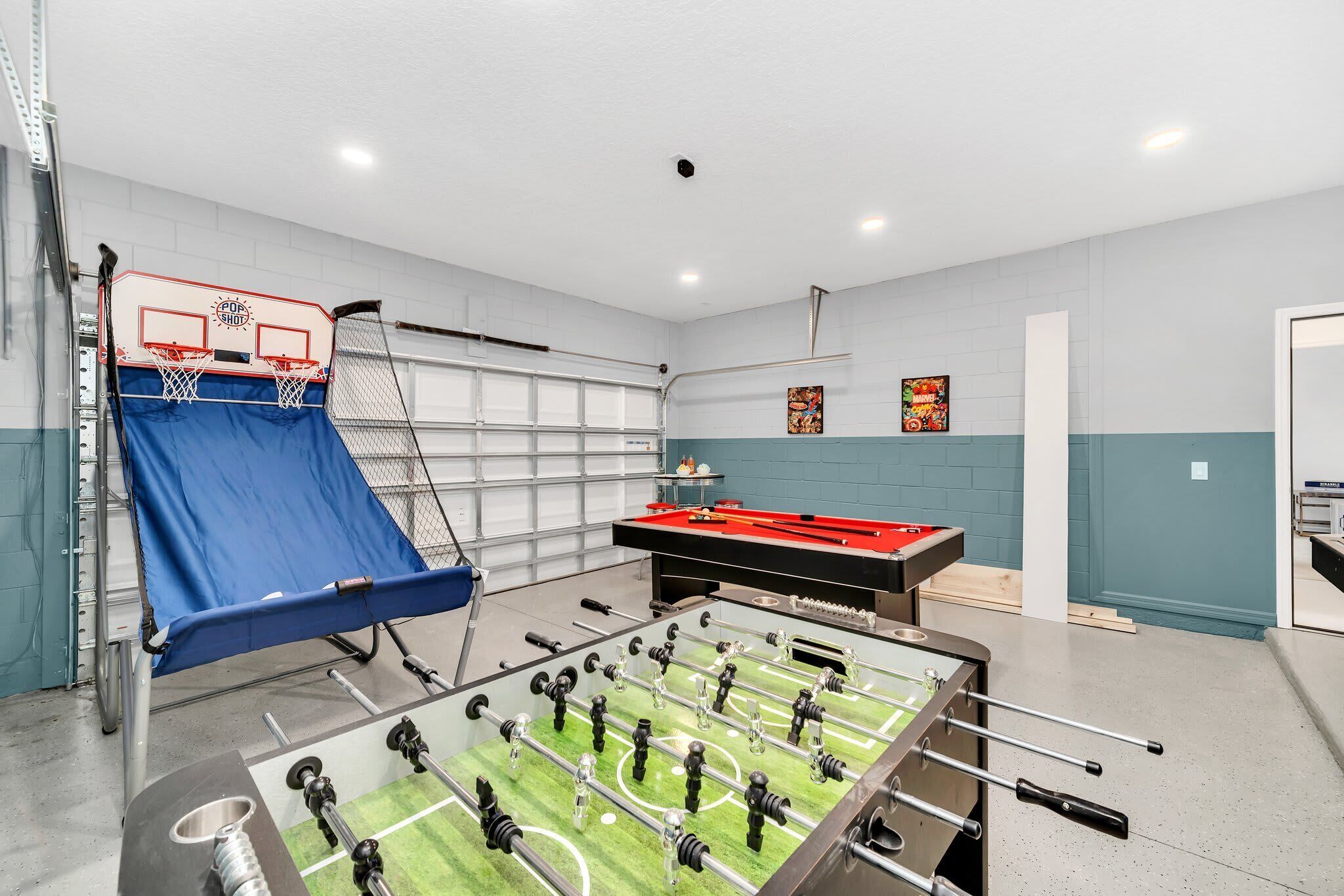 Een kamer met een tafelvoetbaltafel, een poolbiljart en een basketbalring.