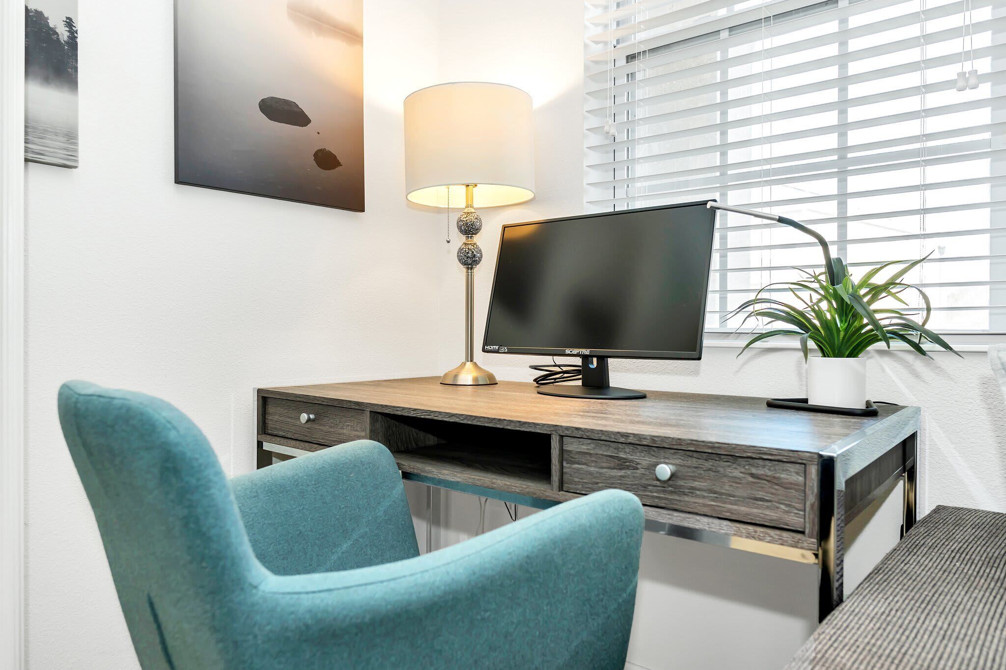 A modern office desk with a computer monitor, a lamp, and a chair.