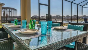 An outdoor dining area with a glass table and wicker chairs, overlooking a scenic view. - Golf Hideaway With Lake View! Modern Decor and Game Room With Multiple Options! #5pr2197 (Davenport)
