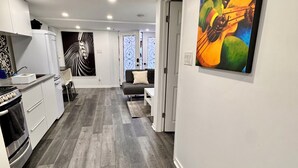 A modern kitchen with white cabinets, a built-in oven, and a dining area with a gray sofa and a small table.