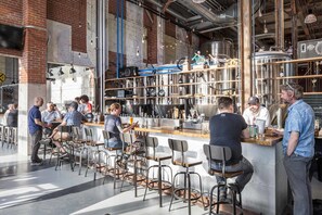 Eine Bar mit Barhocker und Theke, umgeben von Industrie-Dekor und Brauanlage.