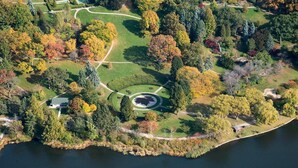 An aerial view of a park with a lake, pathways, and a circular garden area.