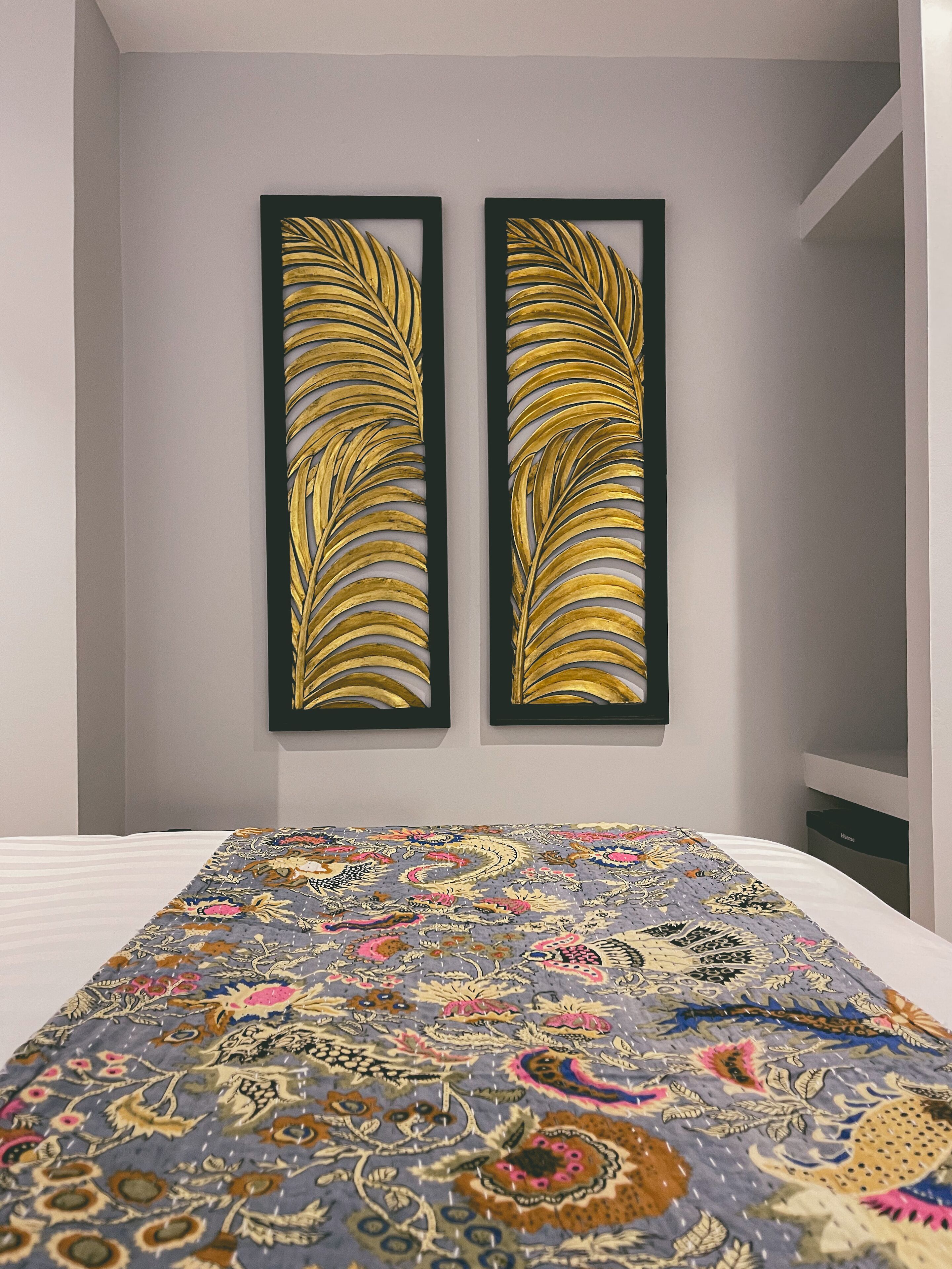 Una habitación con una cama, dos cuadros en la pared y una colcha estampada.