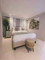 Un dormitorio con una cama, una mesita de noche, una planta en maceta y una obra de arte colgada en la pared.