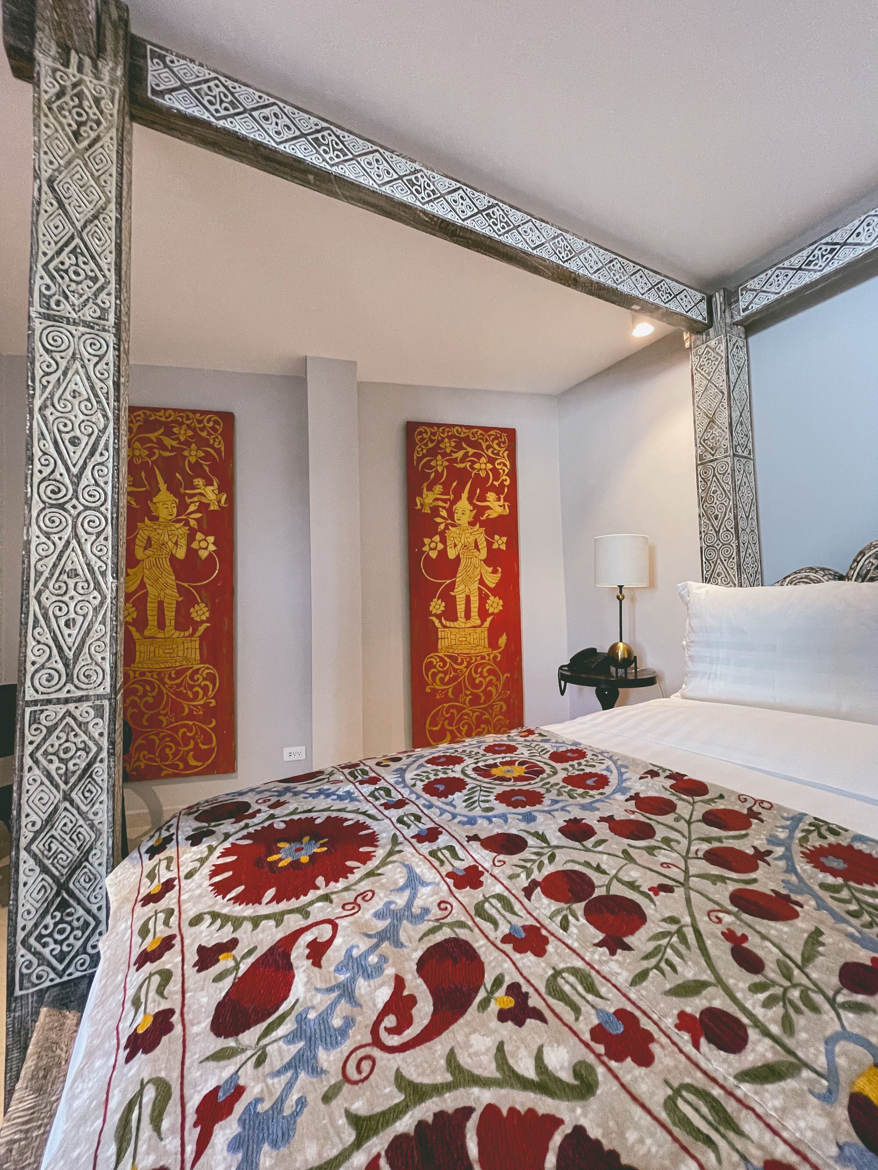 A hotel room with a large bed, decorative wall panels, and a patterned bedspread.