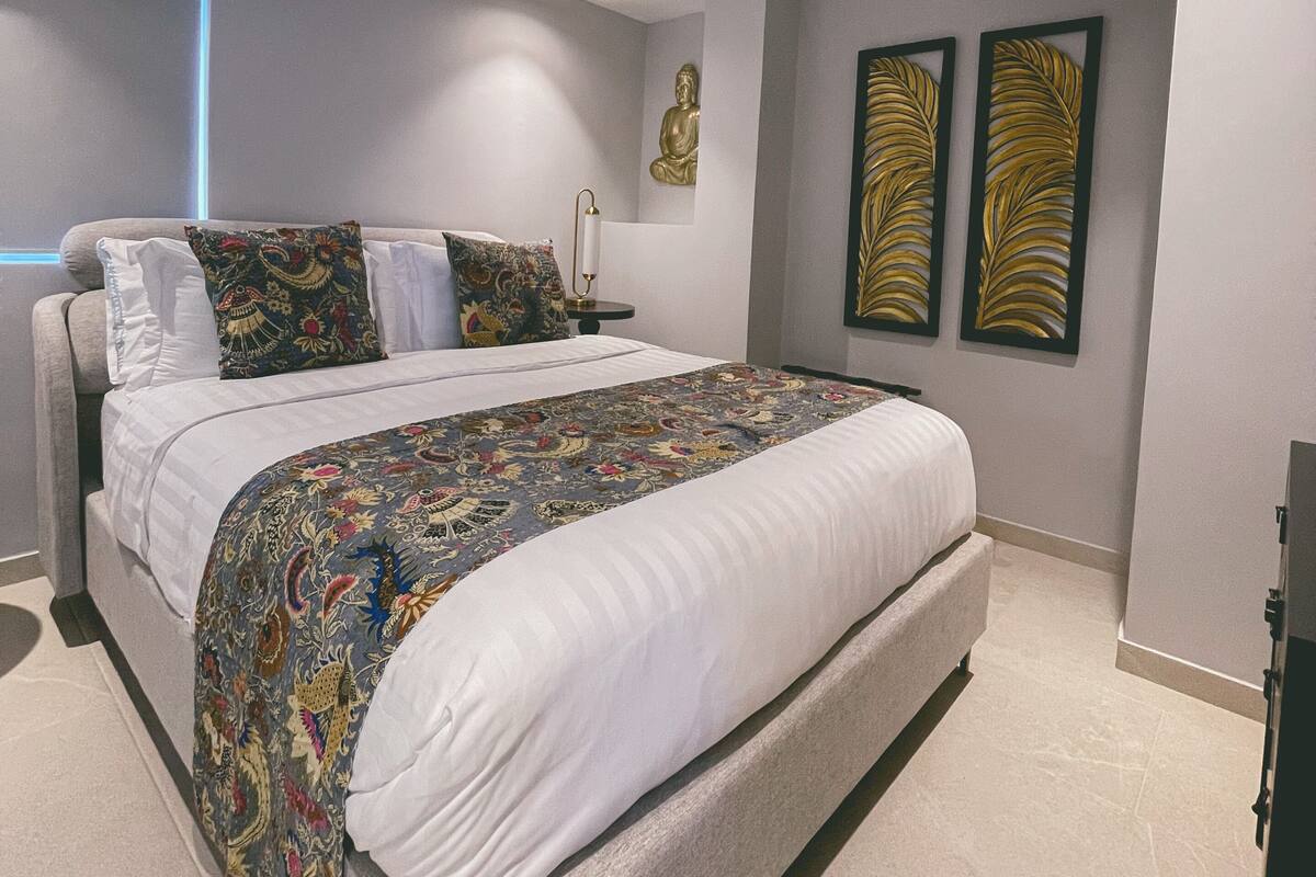 Un dormitorio moderno con una cama grande, una estatua de Buda montada en la pared y dos pinturas abstractas con pan de oro.
