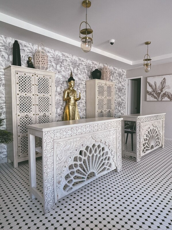 A room with a patterned floor, a central console table with intricate carvings, and a Buddha statue.