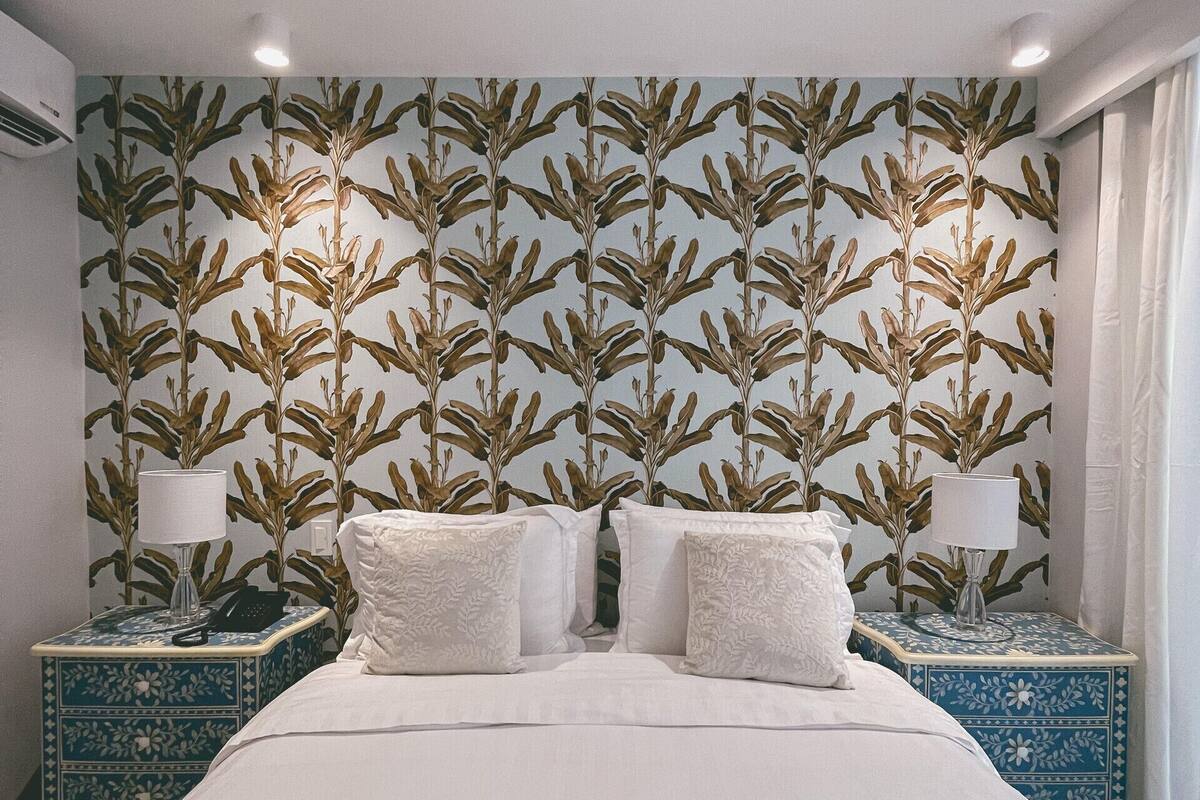 Un dormitorio con una cama grande, dos mesitas de noche con lámparas y un papel tapiz estampado.