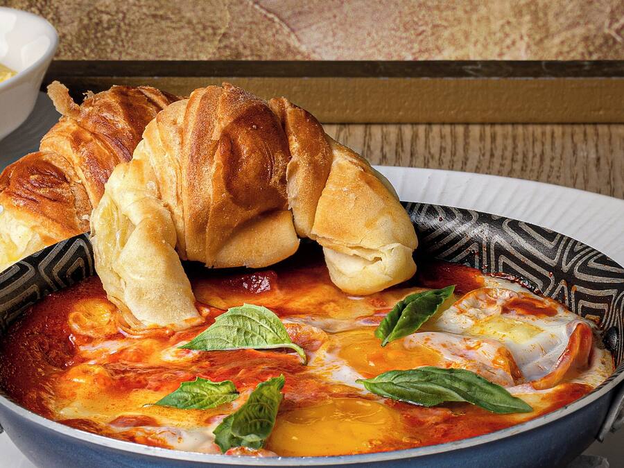 Een kom tomatensoep met kaas en basilicum, vergezeld van een croissant.