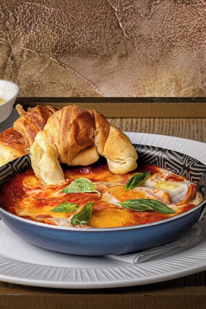 A bowl of tomato-based soup with cheese and basil, accompanied by a croissant. - Hotel Boutique Casa Hendaus - Adults Only (San Andrés)