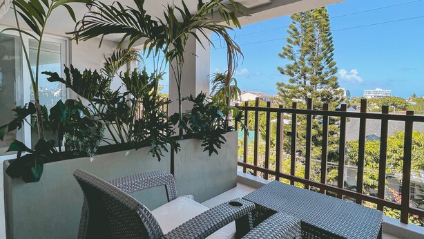 A balcony with wicker furniture and potted plants, overlooking a residential area.