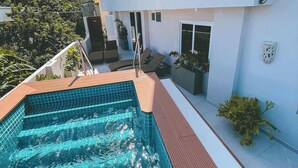 A modern building with a swimming pool, outdoor seating, and potted plants.