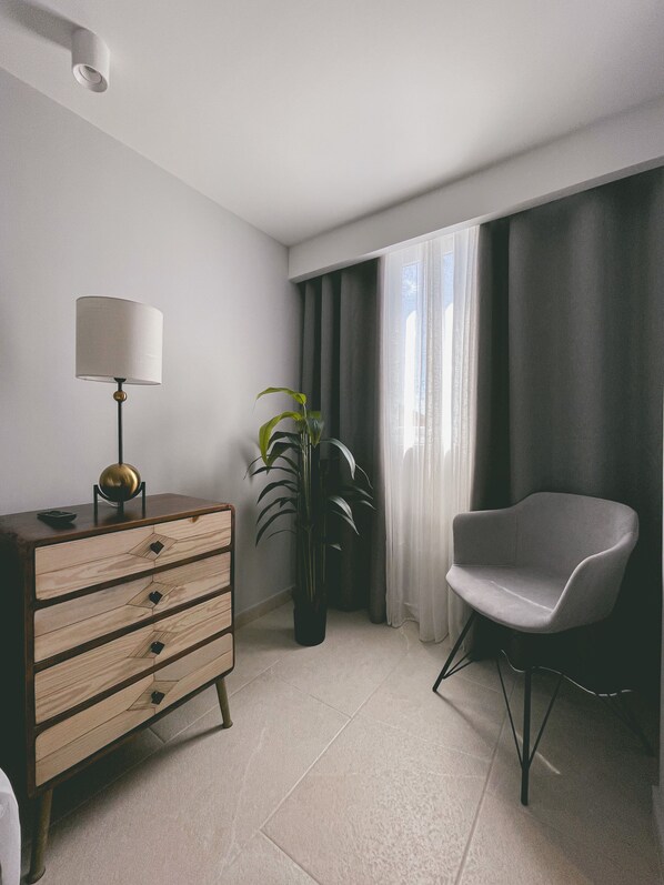 A modern living room with a wooden dresser, a lamp, a chair, and a potted plant.