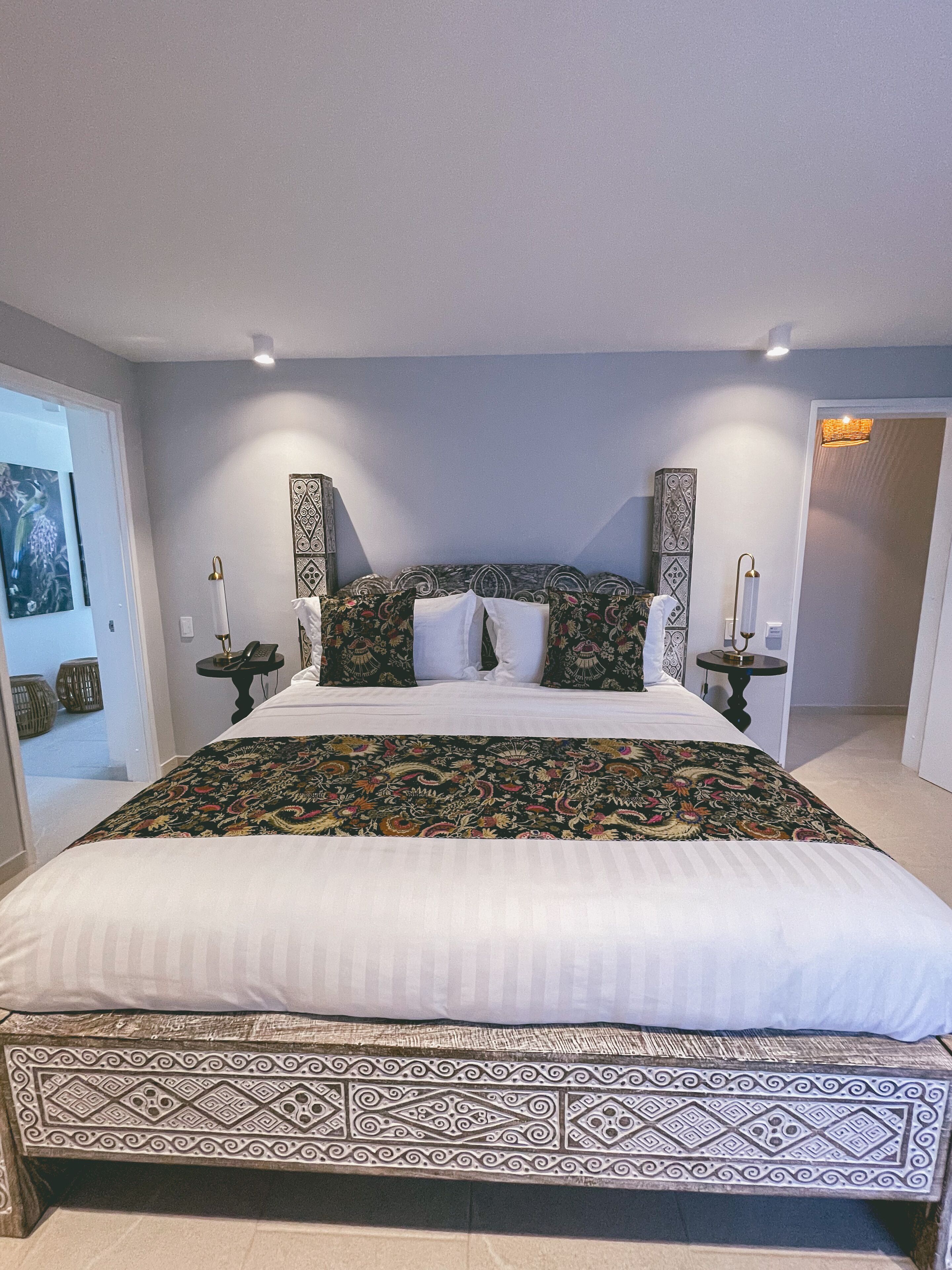 A large bed with a patterned bedspread, two bedside tables with lamps, and a wall with decorative panels.
