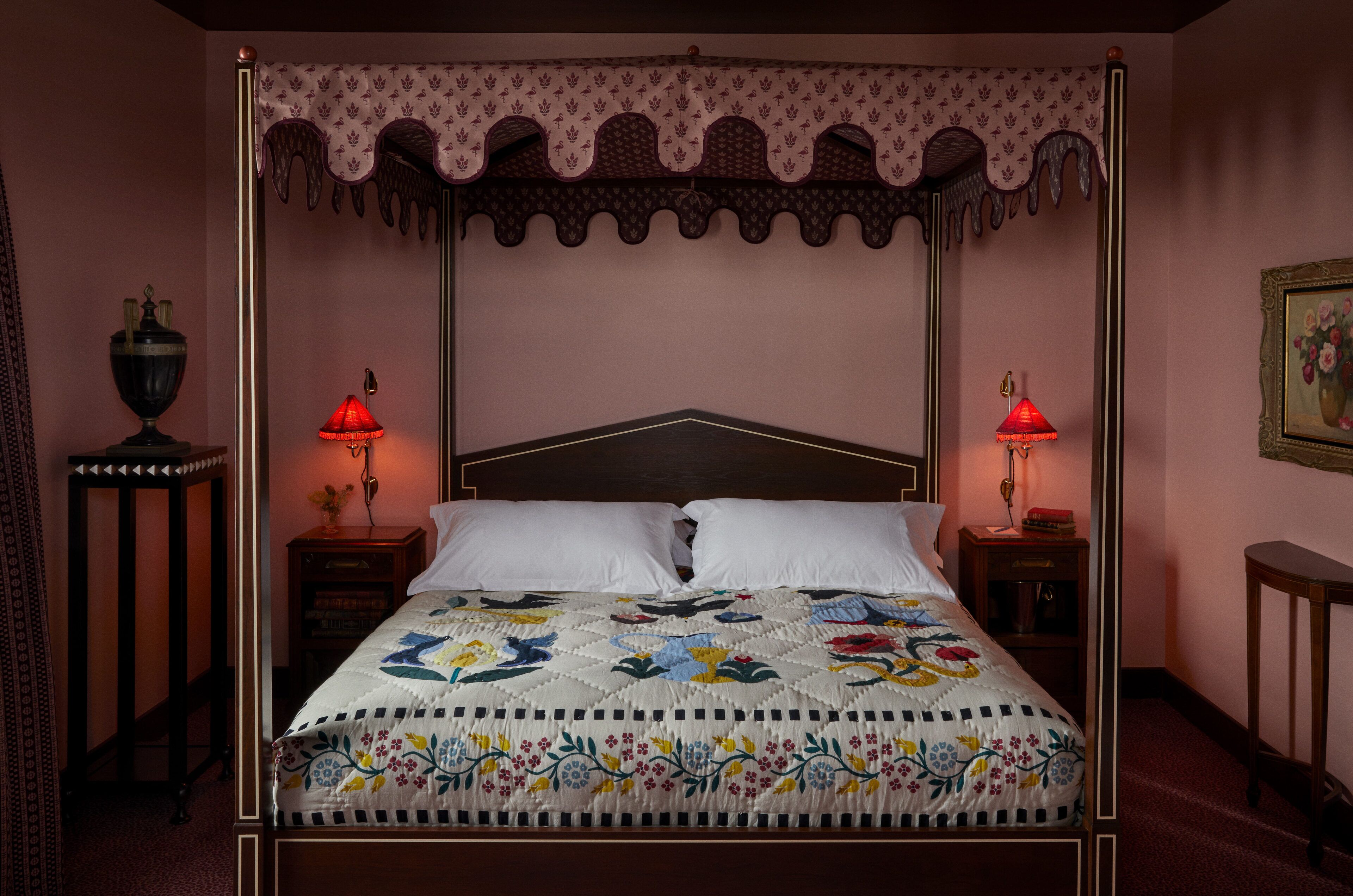 Una cama con dosel adornada con un colcha floral, dos lámparas de noche y un dosel decorativo.