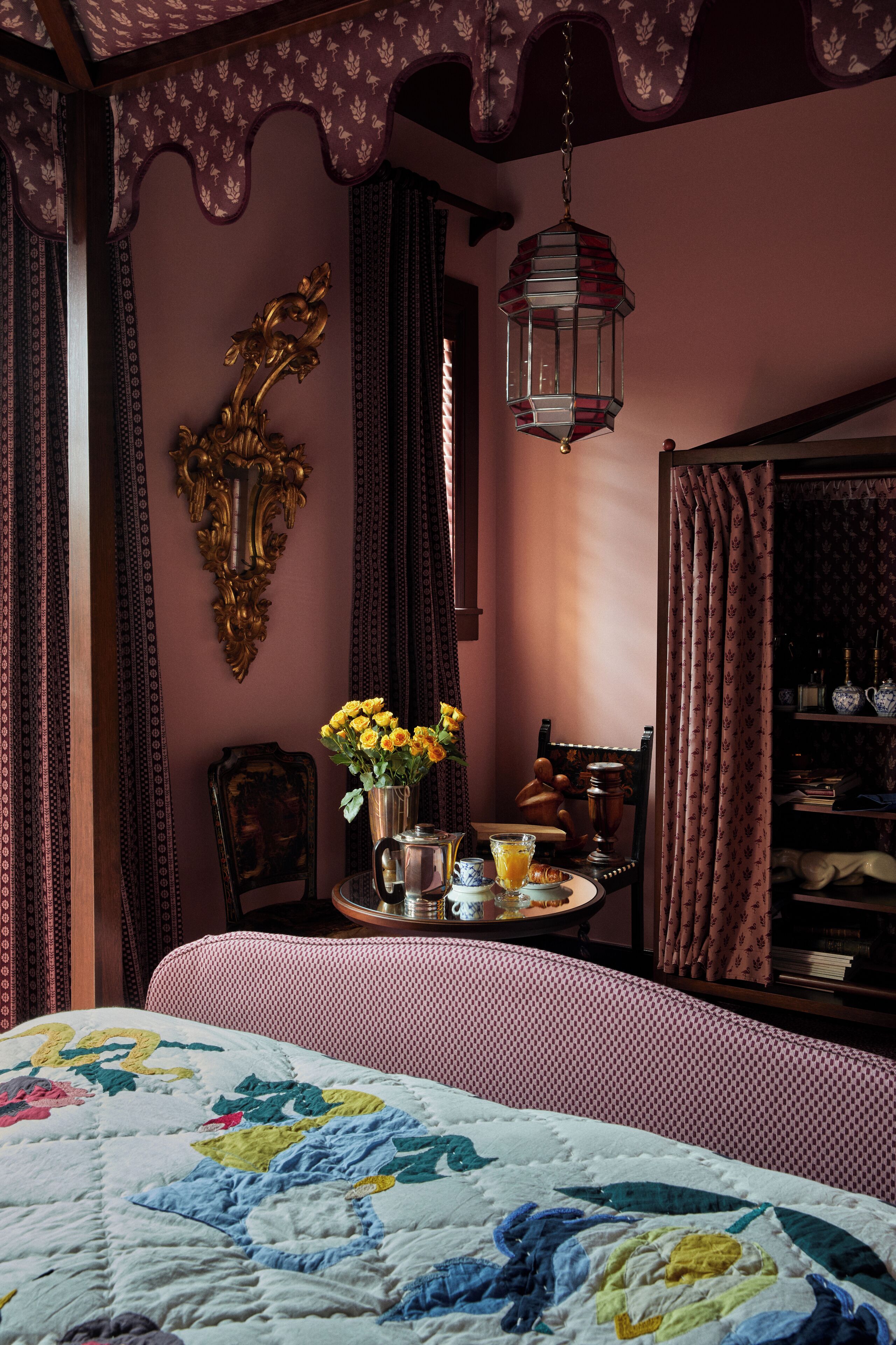 Un dormitorio con una cama, una mesita de noche, un florero con flores, una lámpara y una estantería.