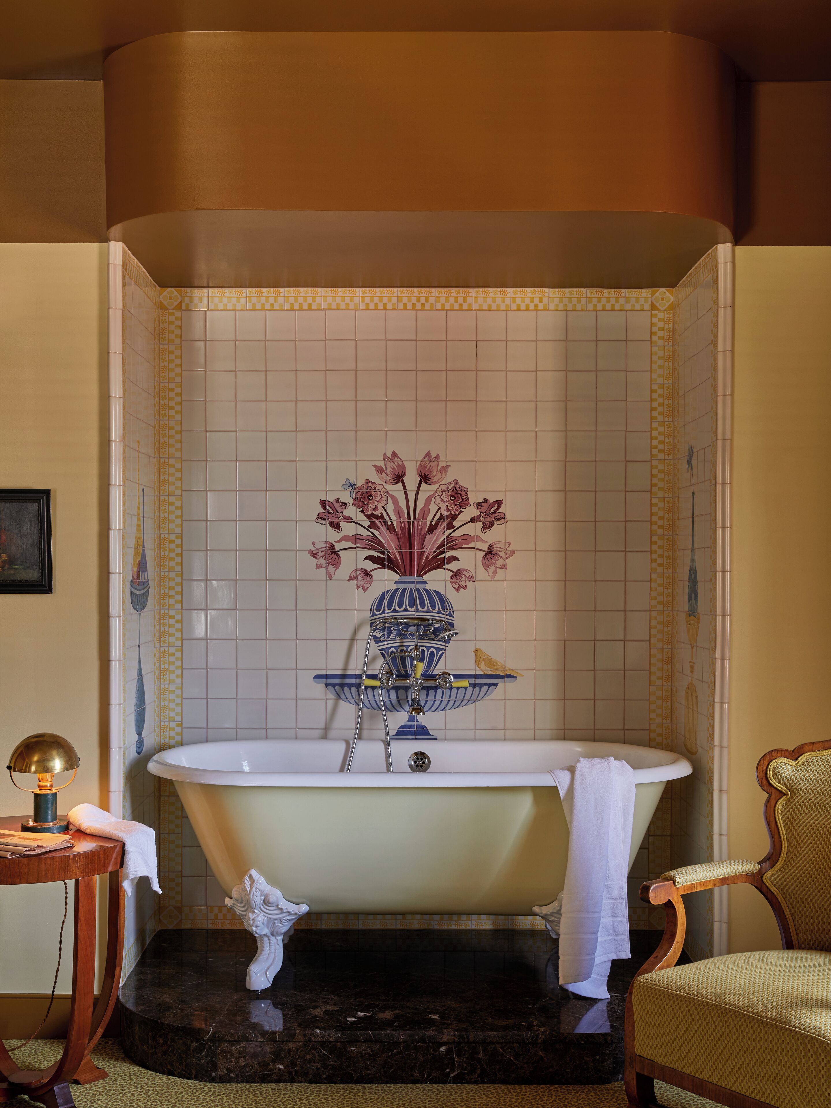 Un baño con una bañera independiente, un jarrón decorativo con flores y un pájaro posado en la pared.