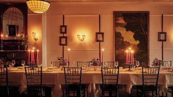 A dining area with tables set for four, each with a candle, framed pictures on the wall, and a chandelier.