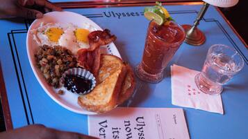 Ein Frühstücksteller mit Eiern, Speck, Toast und einem Bloody Mary auf einem Tisch mit einer Speisekarte.