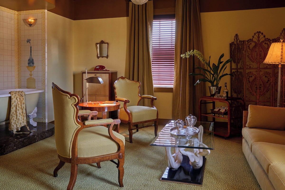 A traditional living room with a sofa, two armchairs, a coffee table, a fireplace, and a window with curtains.