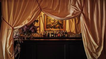 A bar area with a painting on the wall, bottles of alcohol, and a vase of flowers.